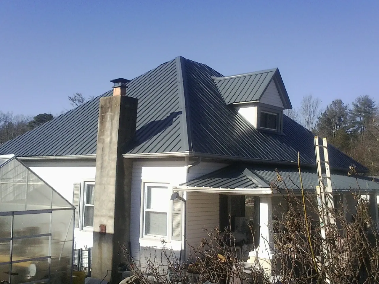 Dark blue standing seam metal roof on a white farmhouse with dormer — Slate & Tile Roof Repair by Roofing Brothers in Albin