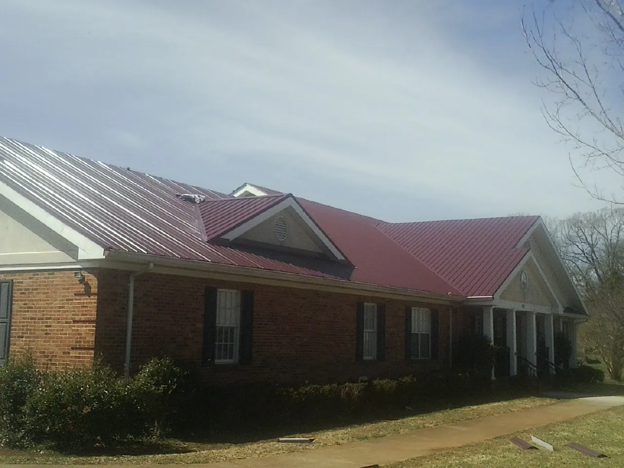 Red metal roof with gabled entries on a long brick building, from a Hail Damage Roof Repair job in Albin