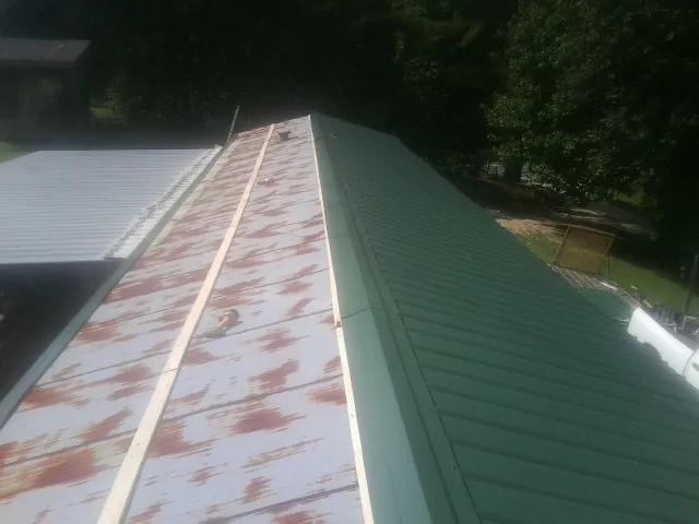 Old rusted panels beside newly installed green metal roofing — Wind Damage Roof Repair by Roofing Brothers in Albin