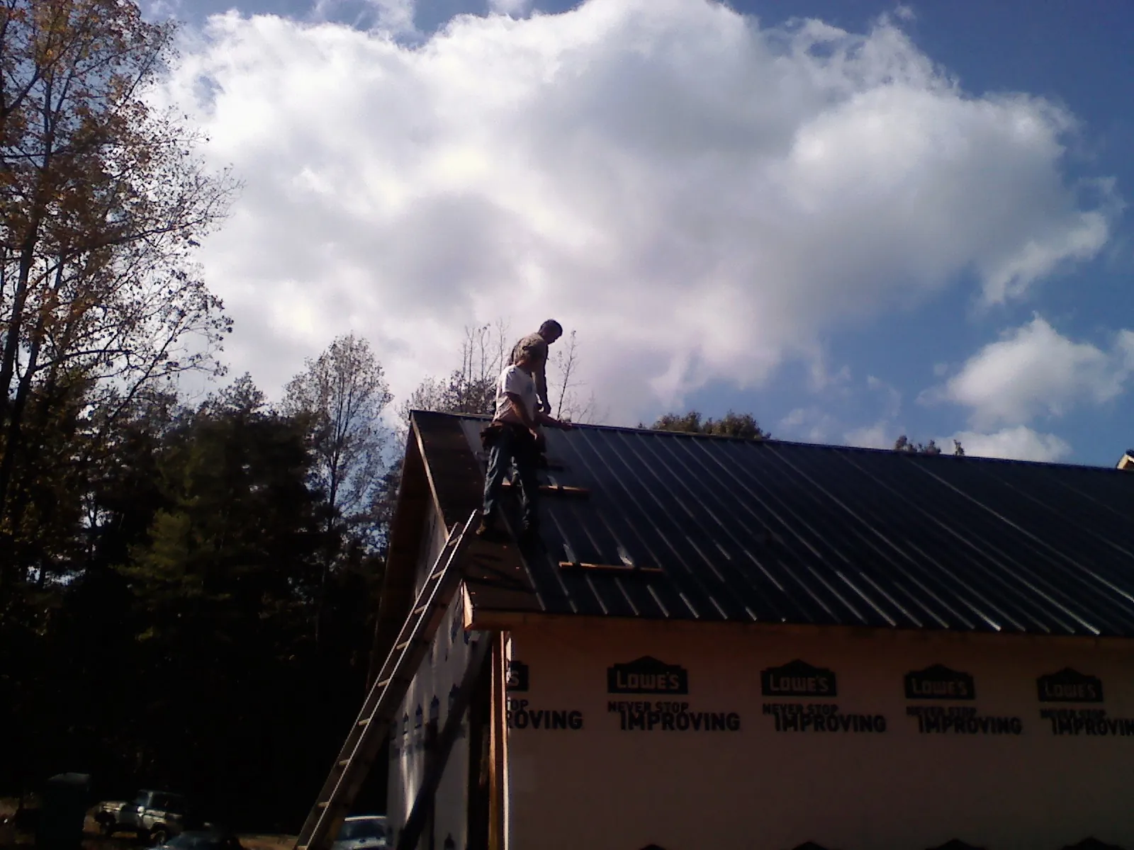 Roofer fastening dark metal panels high against a cloudy sky, from a Roof Inspection job in Albin