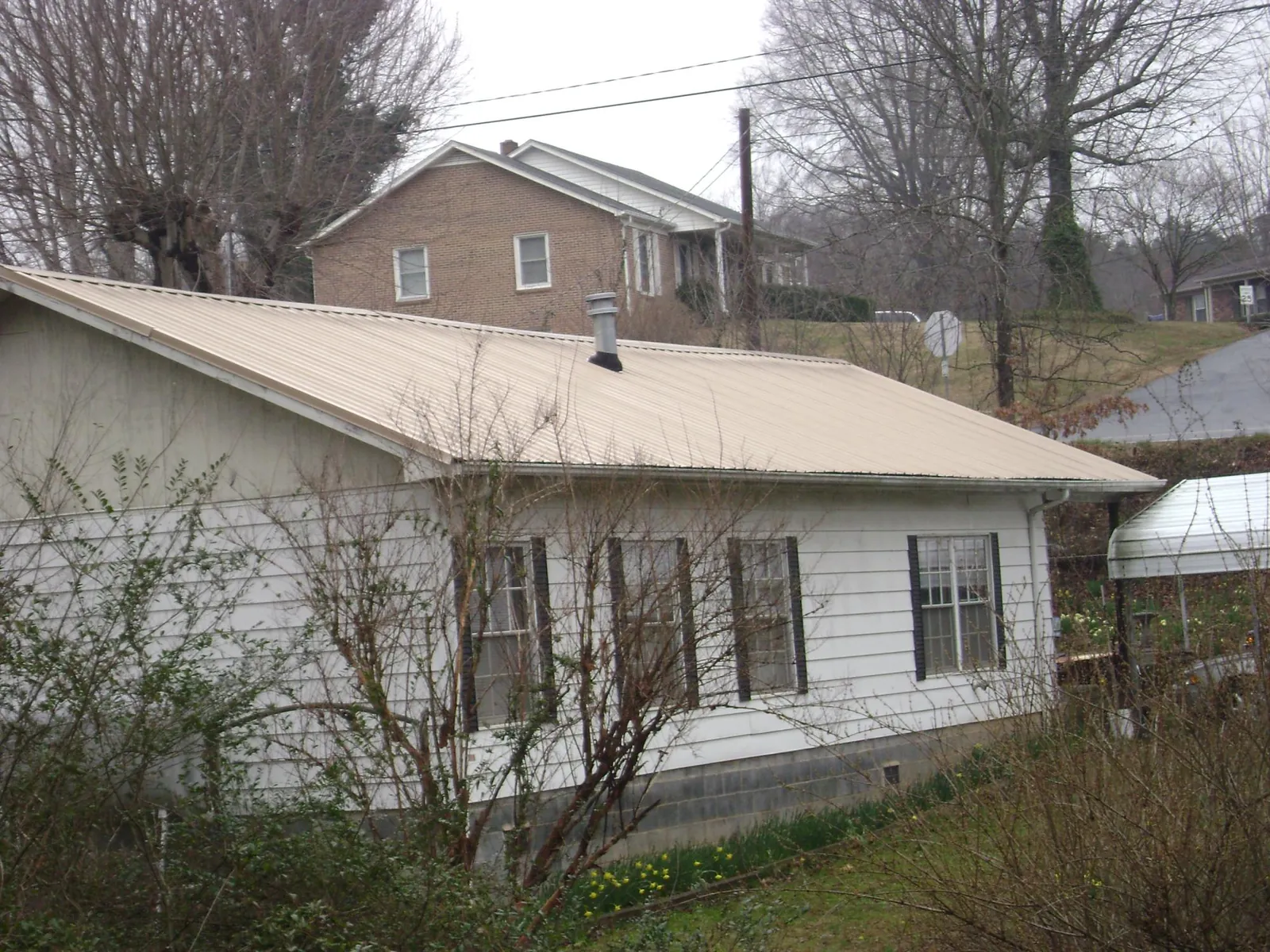 Tan metal roof on a white sided house set into a hillside — Commercial Roofing by Roofing Brothers in Albin