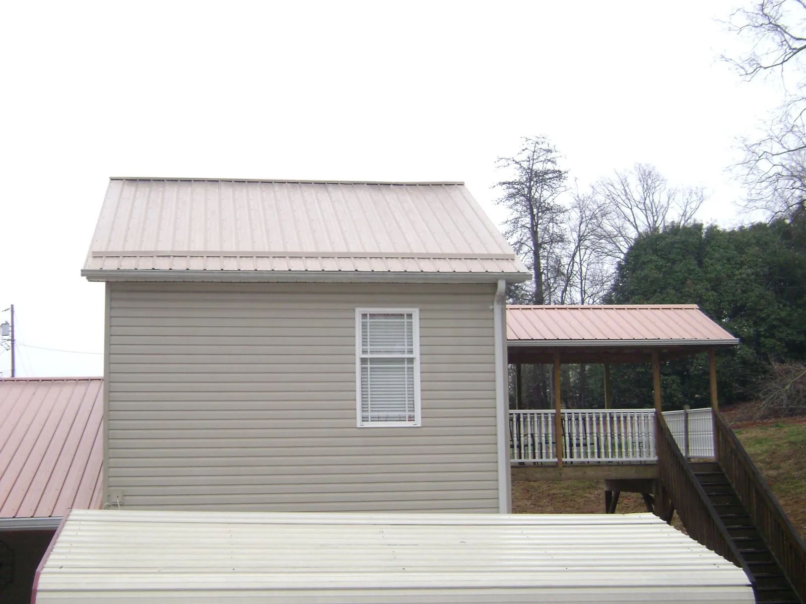 Tan metal roofs on a two story addition and attached porch, from a Roof Replacement job in Albin